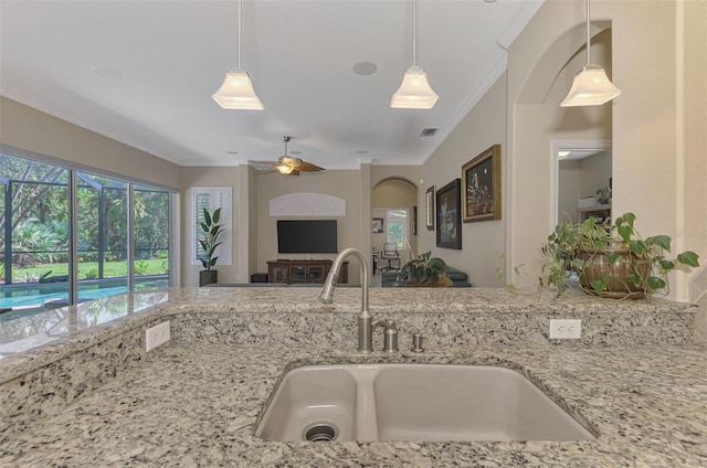 kitchen featuring light stone countertops, ornamental molding, ceiling fan, sink, and pendant lighting