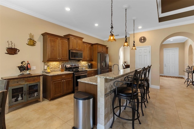 kitchen with stainless steel appliances, light stone countertops, ornamental molding, and a center island with sink