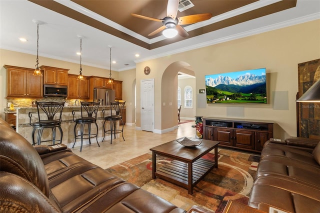 tiled living room with ceiling fan, ornamental molding, and a tray ceiling