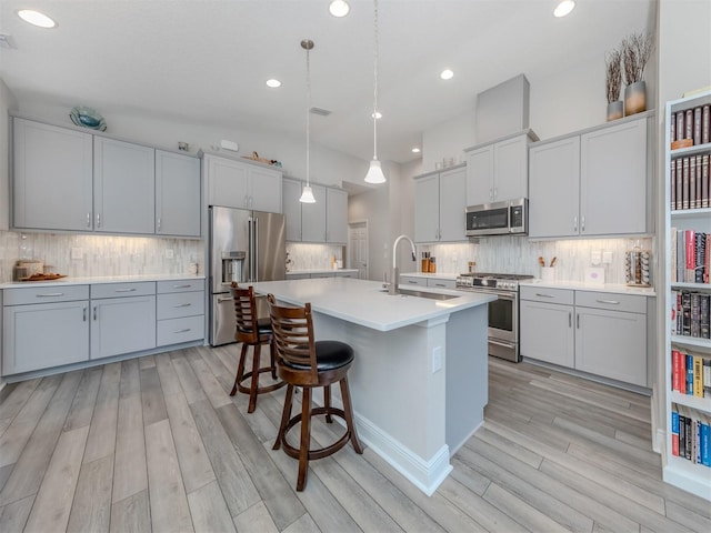 kitchen featuring stainless steel appliances, hanging light fixtures, an island with sink, and light wood-type flooring