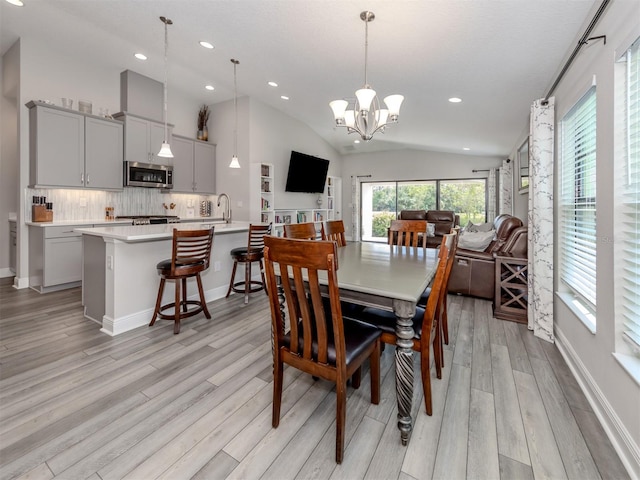 dining area featuring a notable chandelier, light hardwood / wood-style floors, sink, and vaulted ceiling