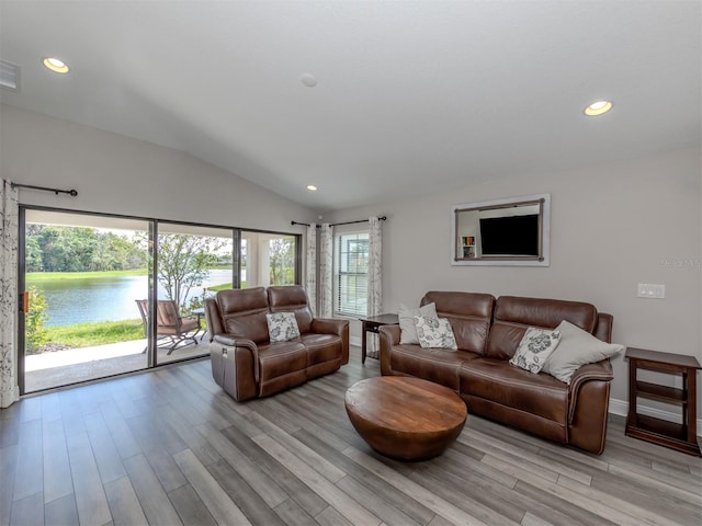 living room with a water view, a wealth of natural light, lofted ceiling, and light wood-type flooring