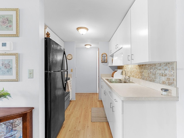 kitchen featuring sink, black fridge, white cabinetry, light wood-type flooring, and backsplash