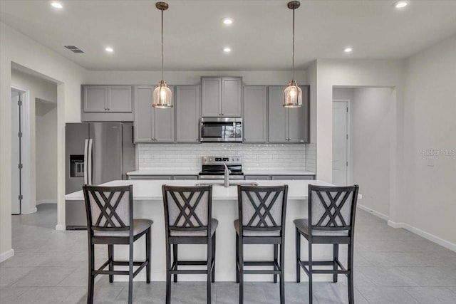 kitchen featuring a center island with sink, decorative light fixtures, gray cabinets, and appliances with stainless steel finishes