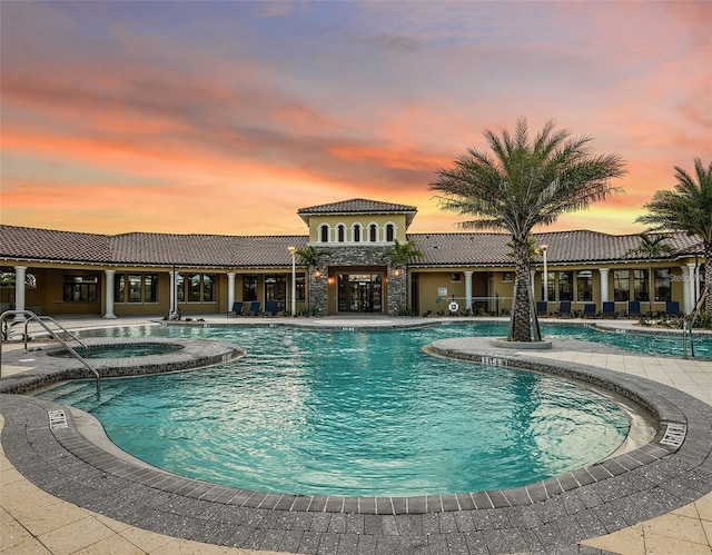 pool at dusk featuring a patio and a hot tub