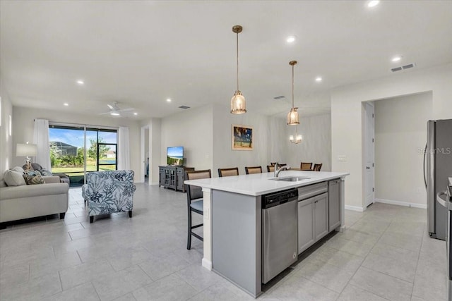 kitchen with a center island with sink, sink, gray cabinets, decorative light fixtures, and stainless steel appliances