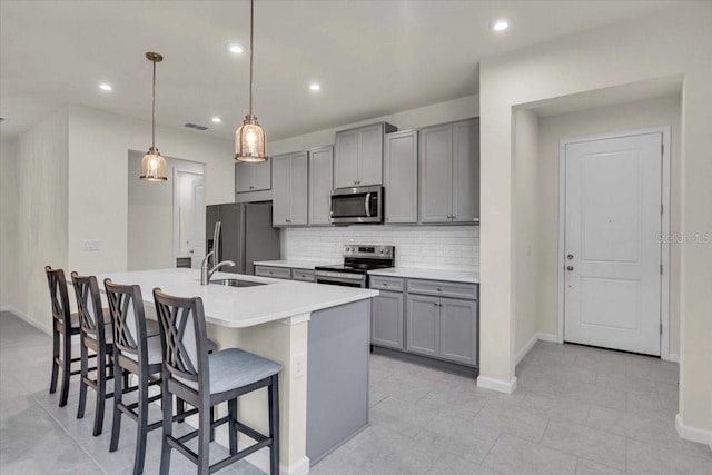 kitchen featuring gray cabinetry, a kitchen breakfast bar, decorative light fixtures, a kitchen island with sink, and appliances with stainless steel finishes