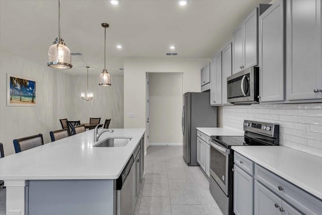 kitchen featuring gray cabinetry, a center island with sink, a kitchen breakfast bar, sink, and appliances with stainless steel finishes