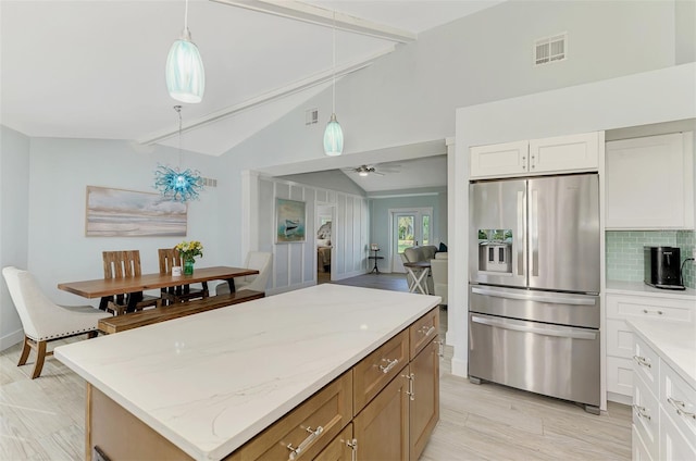 kitchen with white cabinetry, a center island, hanging light fixtures, stainless steel fridge, and vaulted ceiling