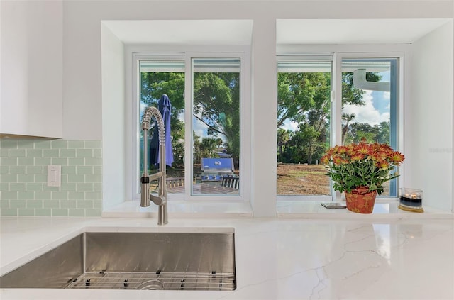 interior details with tasteful backsplash, white cabinetry, sink, and light stone countertops