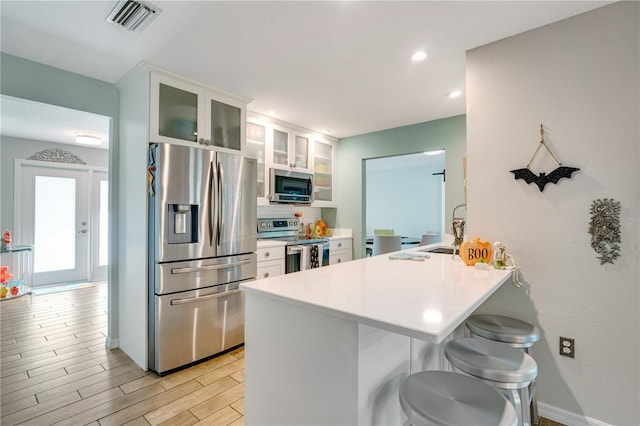 kitchen with appliances with stainless steel finishes, a breakfast bar, kitchen peninsula, white cabinets, and light hardwood / wood-style flooring