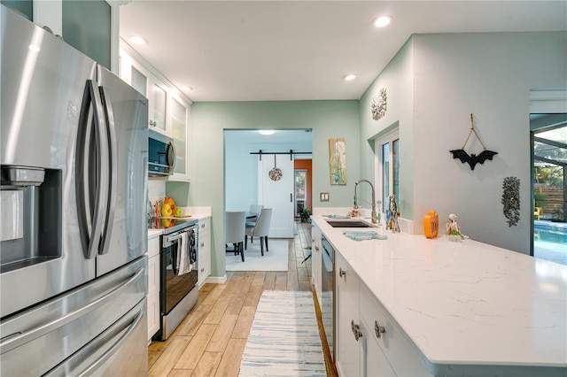 kitchen with sink, a barn door, white cabinetry, stainless steel appliances, and light hardwood / wood-style flooring