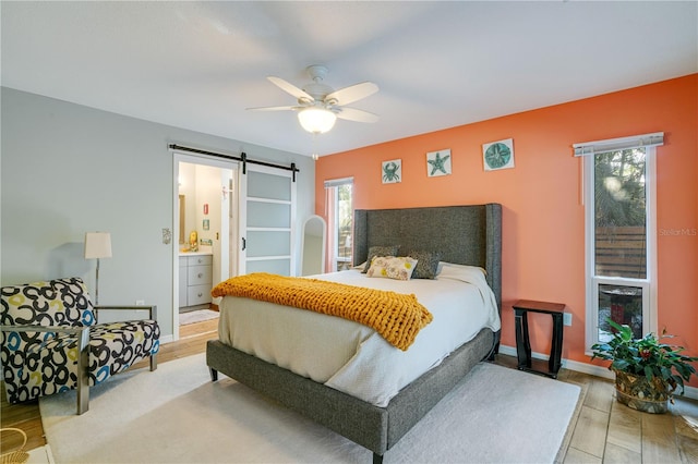 bedroom featuring hardwood / wood-style floors, a barn door, multiple windows, and ceiling fan