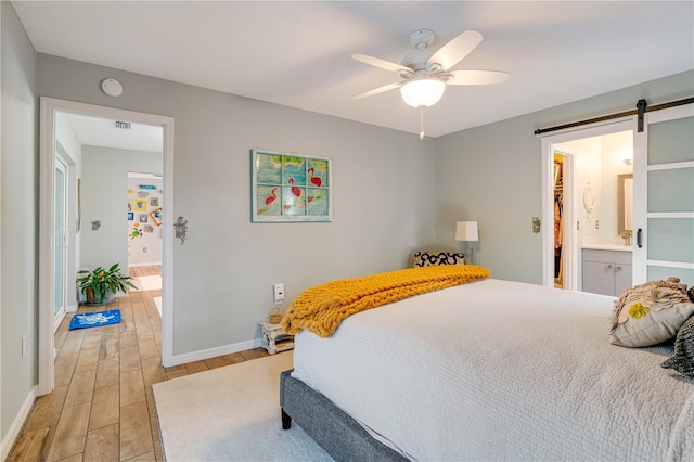 bedroom with ceiling fan, a barn door, light hardwood / wood-style floors, a walk in closet, and ensuite bath