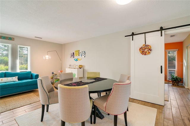 dining space with light hardwood / wood-style flooring, a textured ceiling, a barn door, and a wealth of natural light