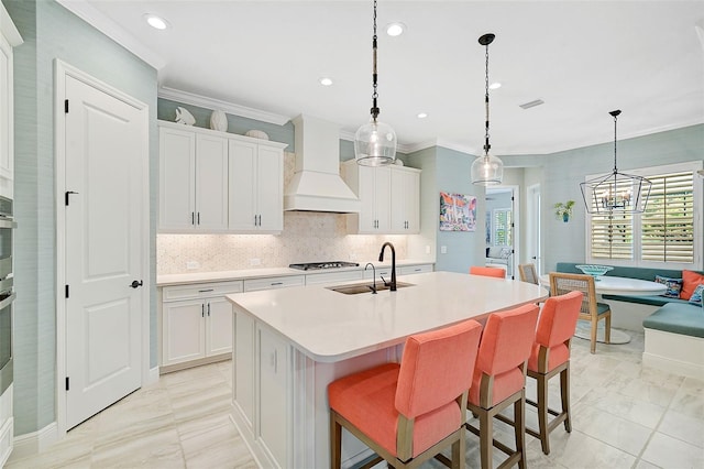 kitchen with pendant lighting, decorative backsplash, an island with sink, white cabinets, and custom exhaust hood