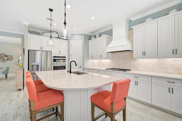 kitchen with sink, appliances with stainless steel finishes, an island with sink, white cabinets, and premium range hood