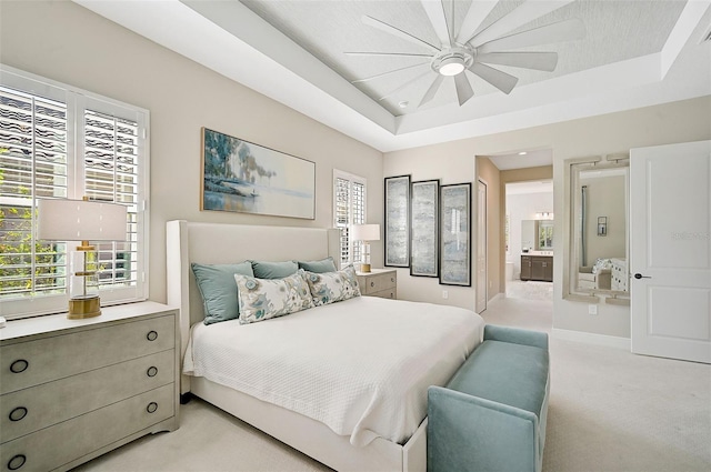 bedroom featuring light colored carpet, a raised ceiling, ceiling fan, and ensuite bathroom