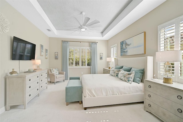 carpeted bedroom featuring a textured ceiling, multiple windows, ceiling fan, and a raised ceiling