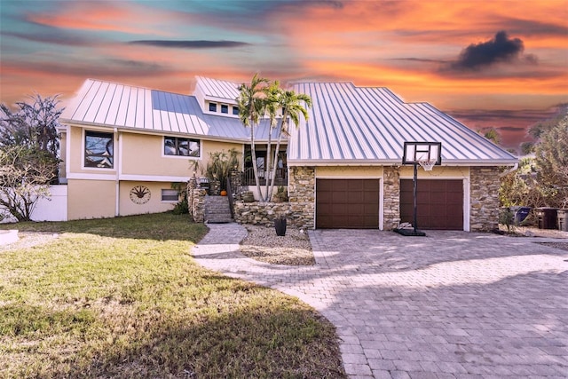 view of front facade featuring a standing seam roof, stone siding, a garage, a lawn, and stucco siding
