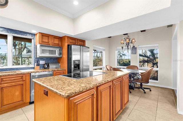 kitchen with appliances with stainless steel finishes, a healthy amount of sunlight, a chandelier, and a kitchen island