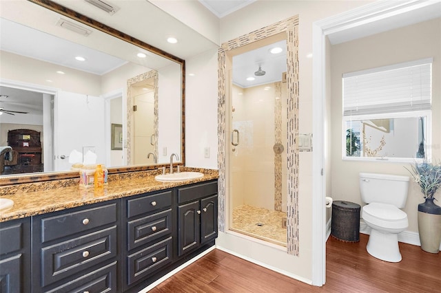 bathroom with toilet, a shower with shower door, wood-type flooring, vanity, and ceiling fan