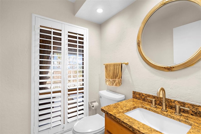 half bathroom featuring toilet, a textured wall, and vanity