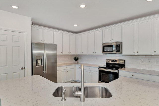 kitchen with sink, white cabinets, appliances with stainless steel finishes, light stone counters, and tasteful backsplash