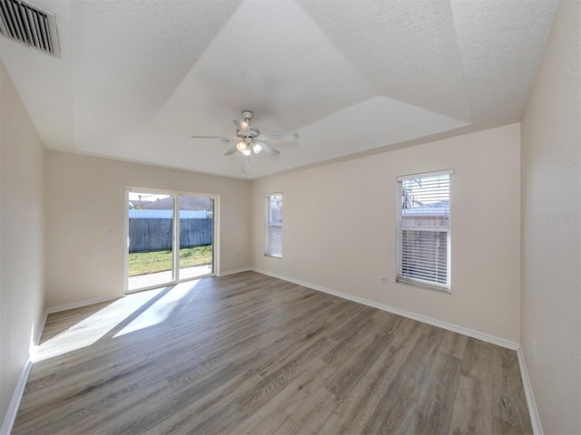 empty room with light hardwood / wood-style flooring, a healthy amount of sunlight, a raised ceiling, and ceiling fan