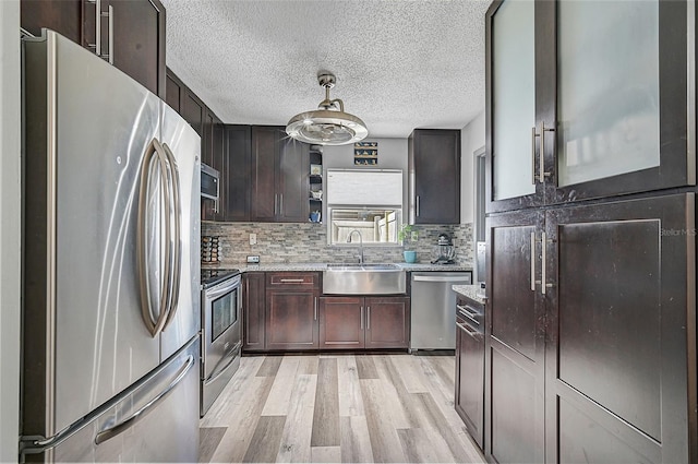 kitchen featuring stainless steel appliances, backsplash, sink, a textured ceiling, and light hardwood / wood-style floors