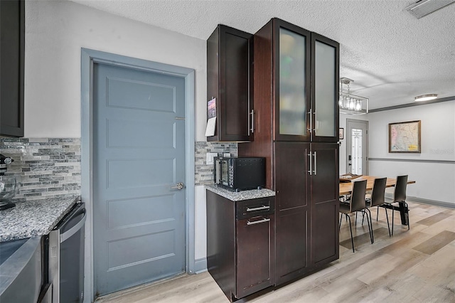 kitchen with light stone countertops, light hardwood / wood-style floors, decorative backsplash, and a textured ceiling