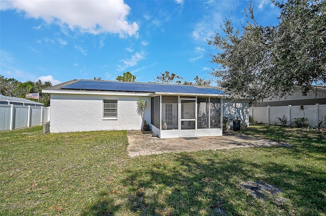 back of property with a patio, a sunroom, a lawn, and solar panels