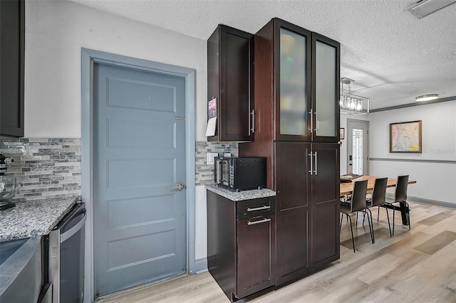 6738 Brentford Rd, Sarasota, FL 34241 - kitchen with light wood-style floors, a textured ceiling, decorative backsplash, light stone counters, and glass insert cabinets