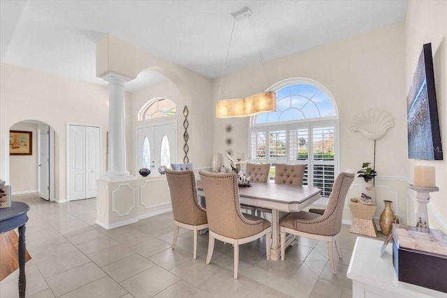 dining area featuring ornate columns, light tile patterned floors, a high ceiling, and french doors