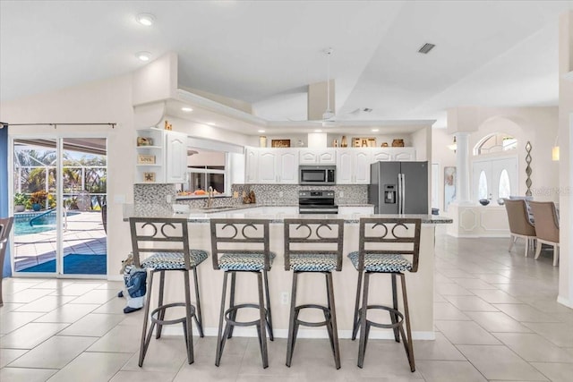 kitchen with appliances with stainless steel finishes, vaulted ceiling, sink, white cabinets, and a breakfast bar area