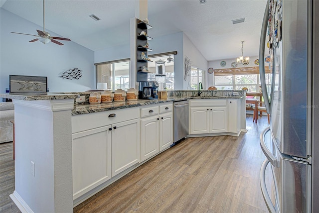 kitchen featuring kitchen peninsula, lofted ceiling, white cabinetry, dark stone counters, and stainless steel appliances