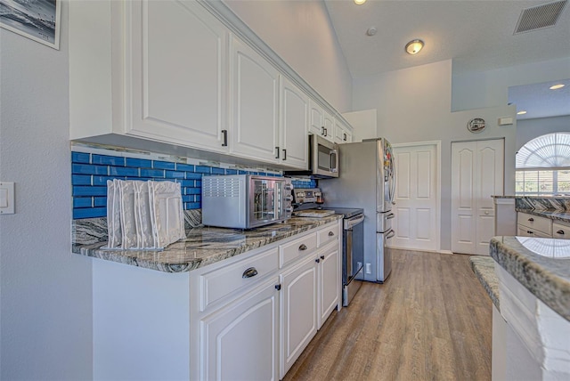 kitchen featuring dark stone countertops, stainless steel appliances, tasteful backsplash, and white cabinets