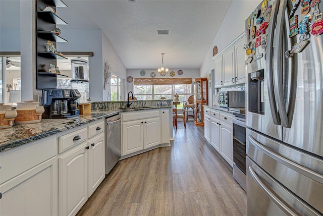 kitchen with white cabinets, light wood-type flooring, vaulted ceiling, pendant lighting, and stainless steel appliances