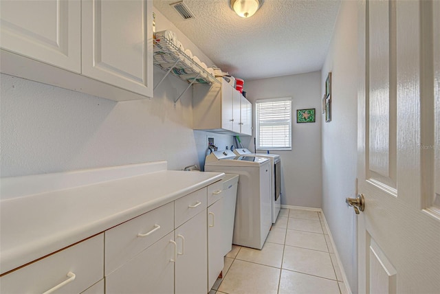 laundry area featuring cabinets, washer and dryer, a textured ceiling, and light tile patterned floors