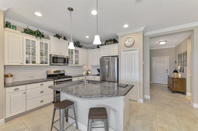 kitchen with a kitchen island with sink, stainless steel appliances, dark stone counters, ornamental molding, and sink