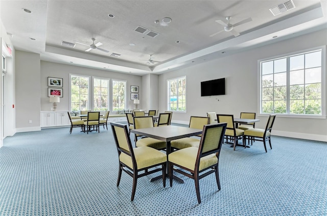 carpeted dining room featuring ceiling fan and a raised ceiling