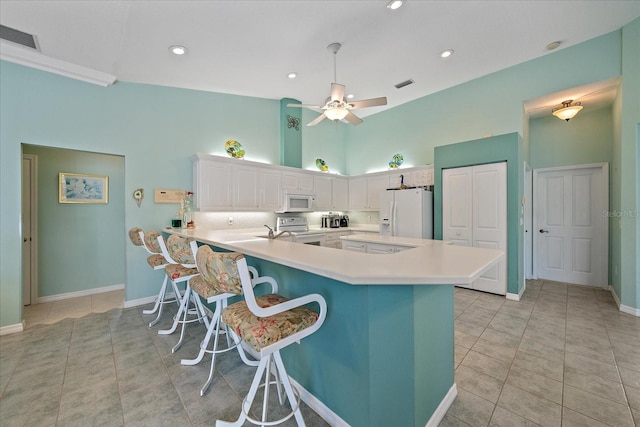 kitchen with kitchen peninsula, white cabinets, ceiling fan, a kitchen breakfast bar, and white appliances