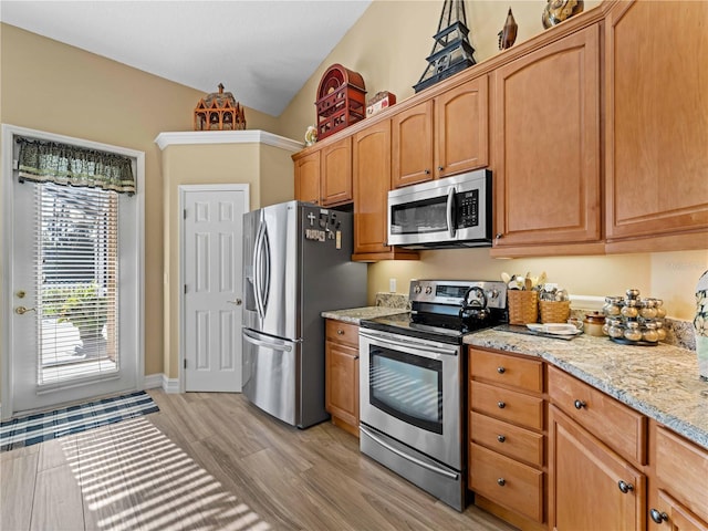 kitchen with lofted ceiling, light hardwood / wood-style flooring, light stone counters, and stainless steel appliances