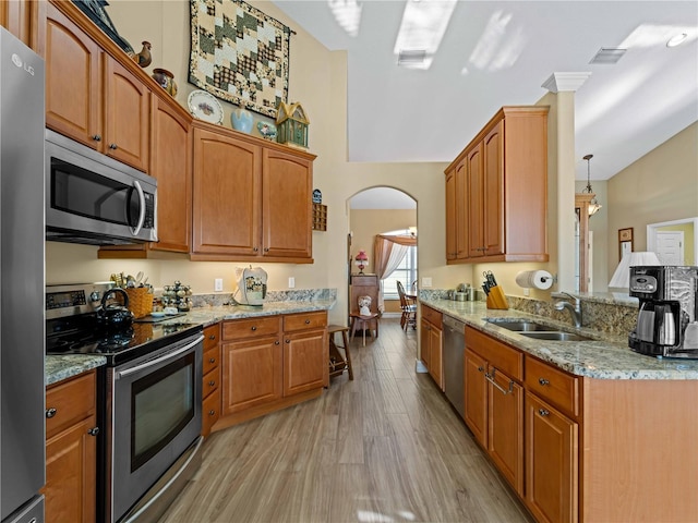 kitchen featuring sink, pendant lighting, appliances with stainless steel finishes, light stone counters, and light hardwood / wood-style floors