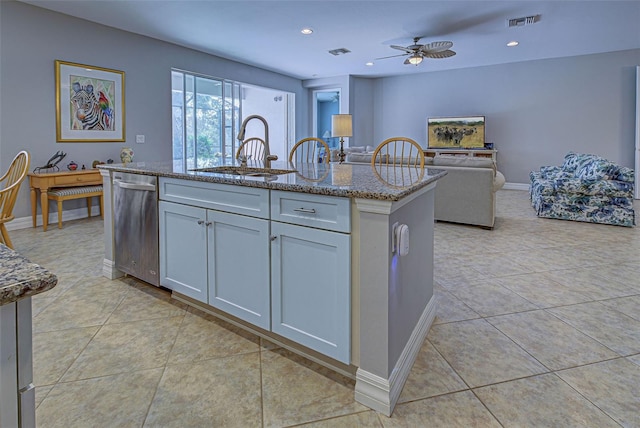 kitchen featuring a center island with sink, sink, light stone countertops, light tile patterned floors, and white cabinets