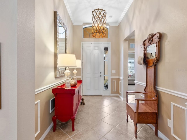 tiled entrance foyer featuring ornamental molding and a chandelier