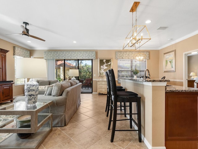 kitchen featuring ceiling fan with notable chandelier, dark stone countertops, ornamental molding, a kitchen bar, and decorative light fixtures