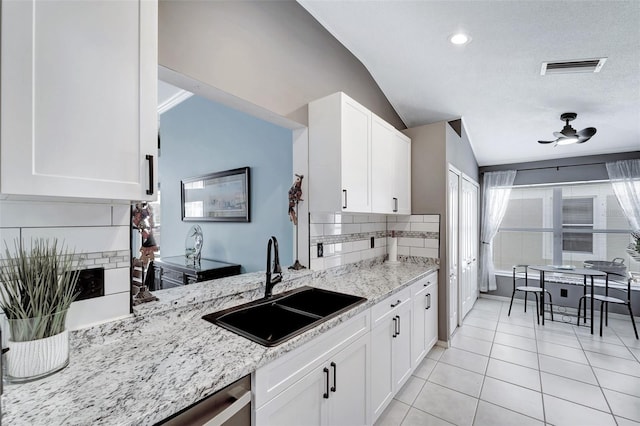 kitchen featuring white cabinets, light stone counters, sink, and vaulted ceiling