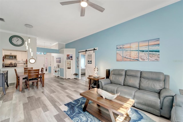 living room featuring a barn door, ceiling fan, light hardwood / wood-style flooring, and ornamental molding