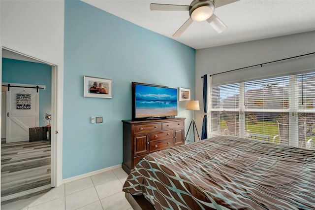 bedroom featuring light tile patterned floors, a barn door, and ceiling fan